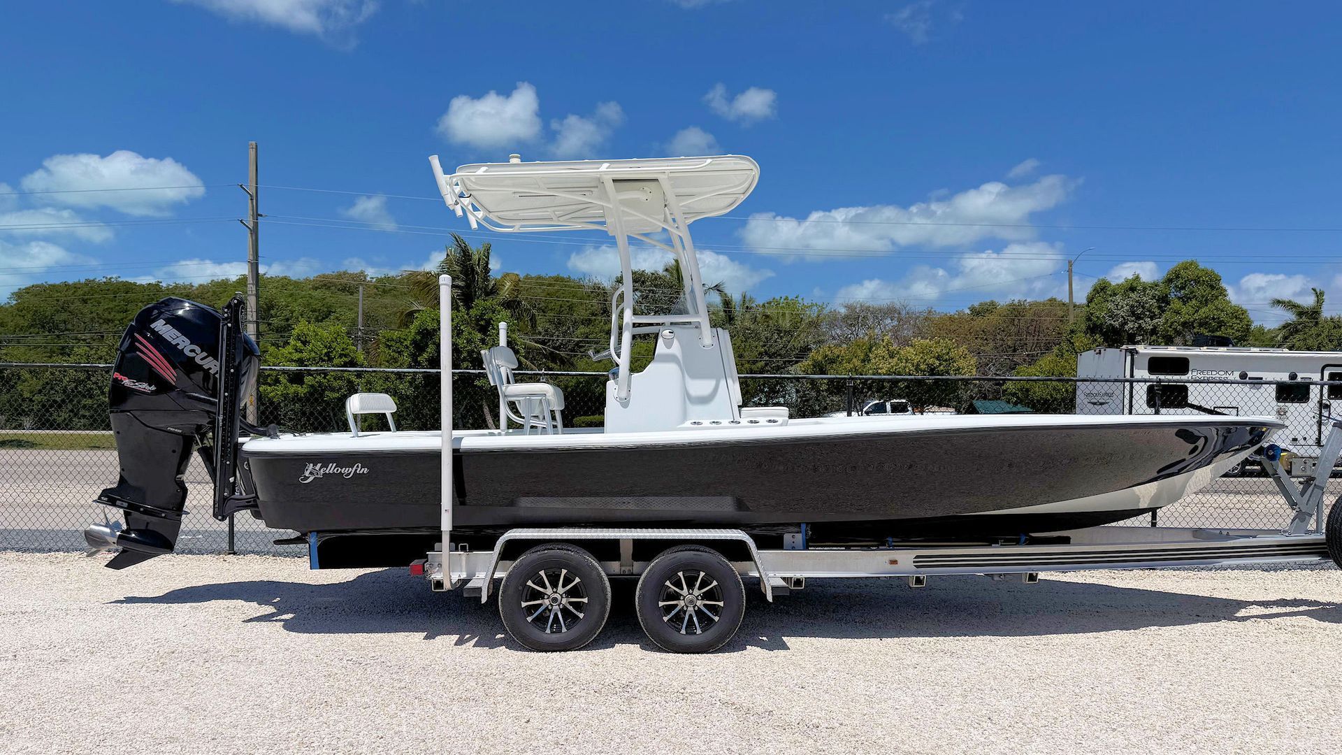 A black and white center console boat on a trailer, parked on a gravel lot under a clear blue sky.