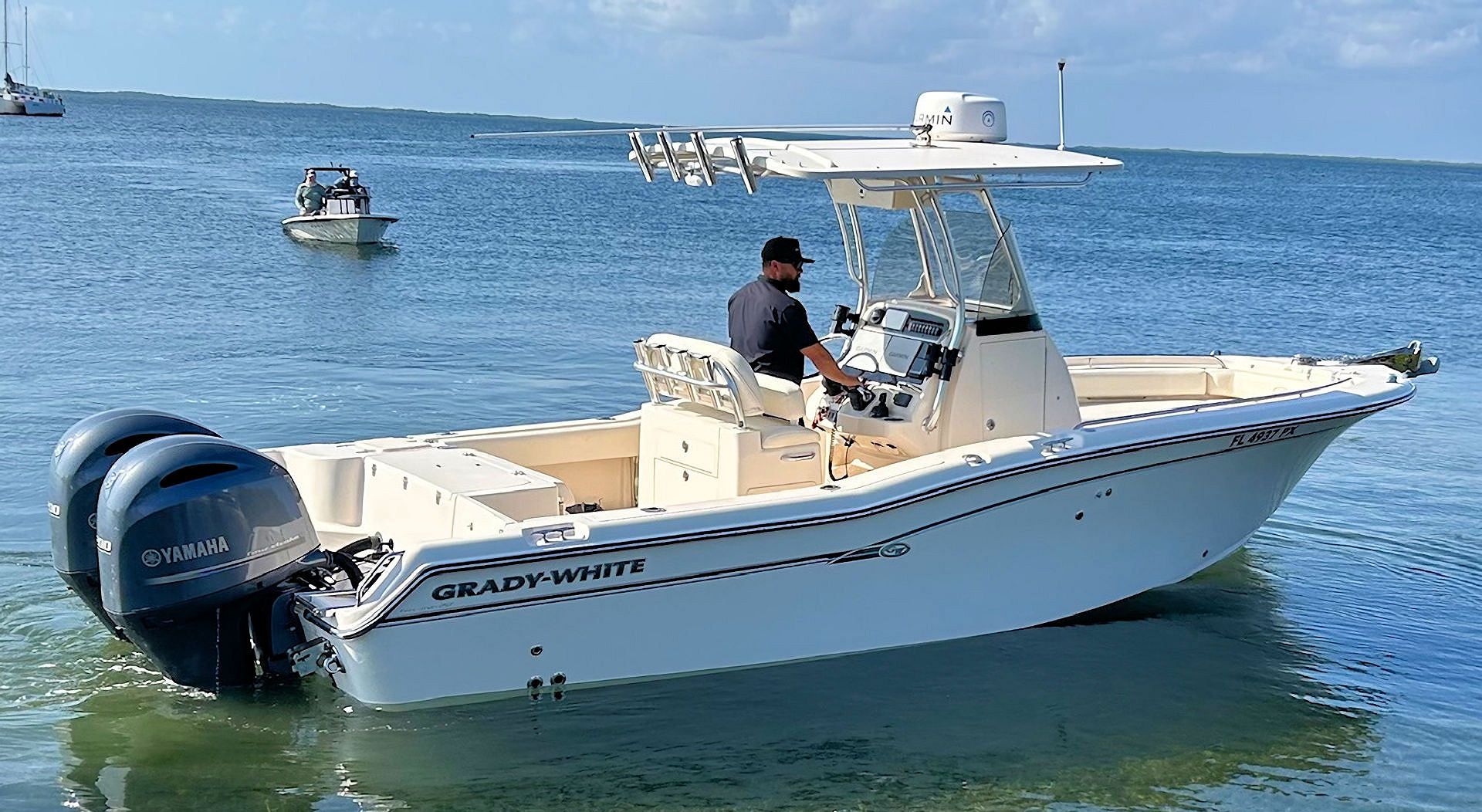 A white center console boat with two outboard motors travels across open water with a person at the helm.