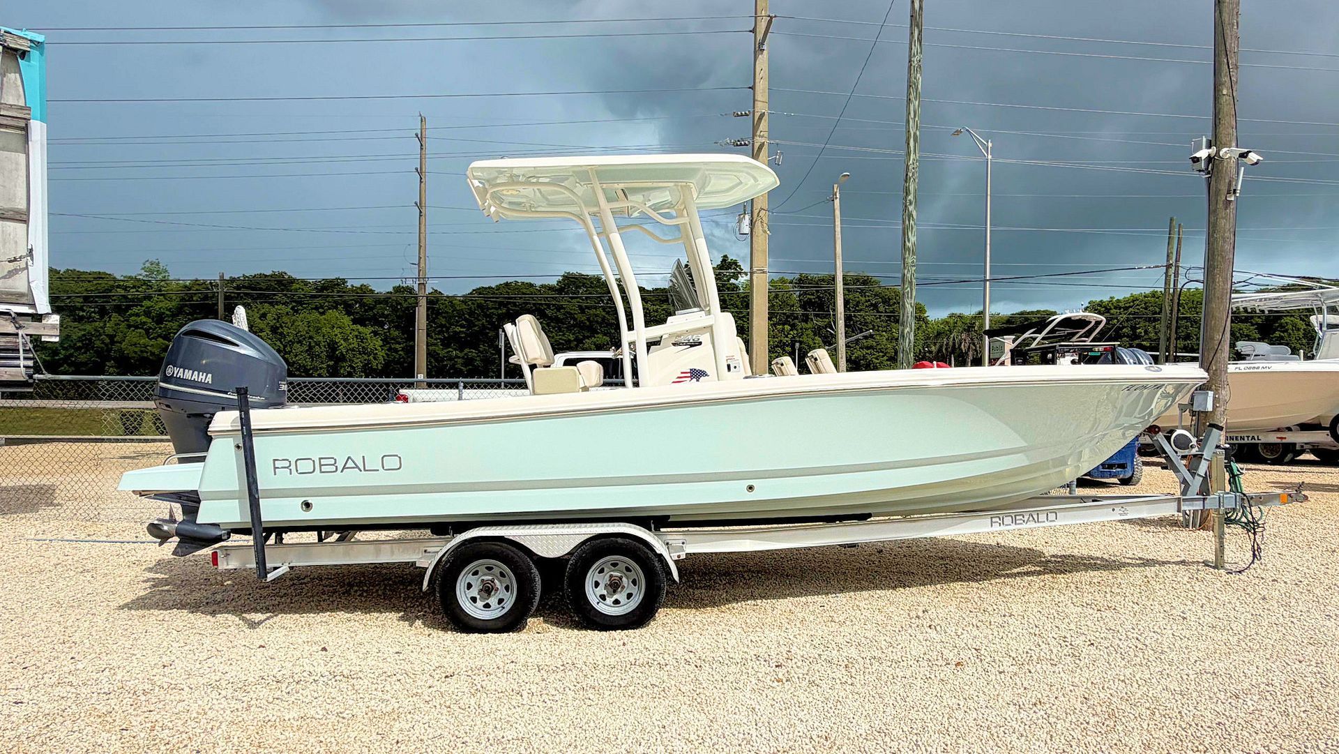 Light blue bay fishing boat on a trailer parked on gravel near the water