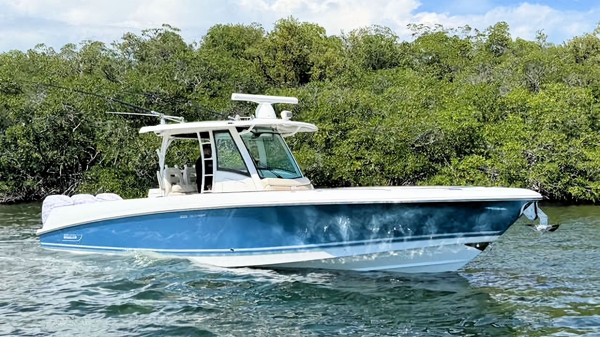 Blue-and-white Boston Whaler center console boat on calm water with green shoreline in the background
