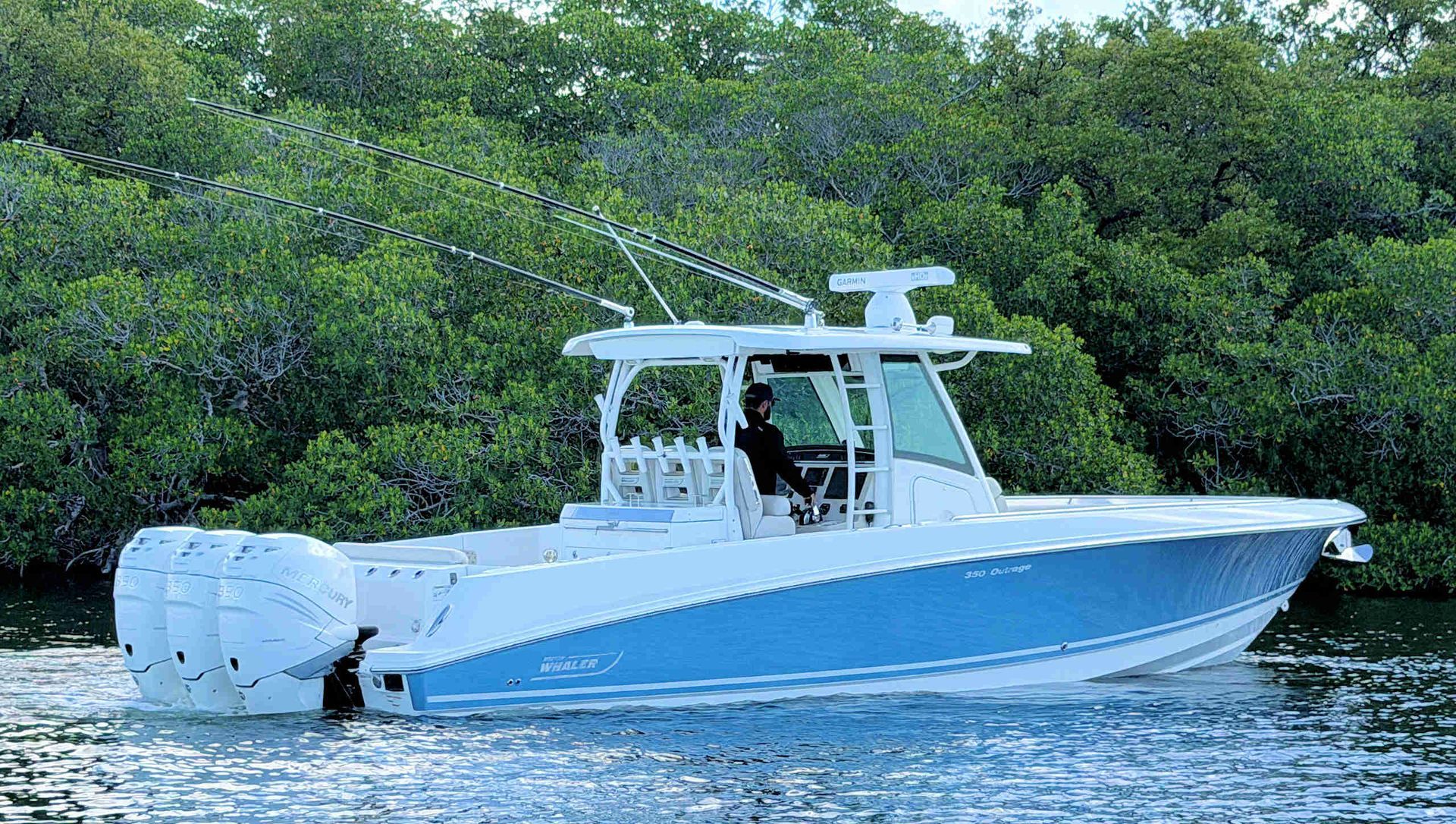 White center-console boat cruising on calm water near a green shoreline