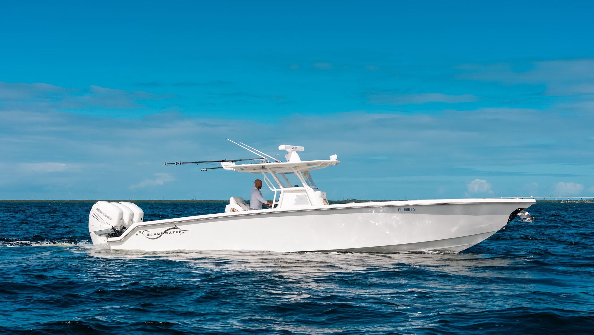 A white center console powerboat cruising across the blue ocean under a clear sky.