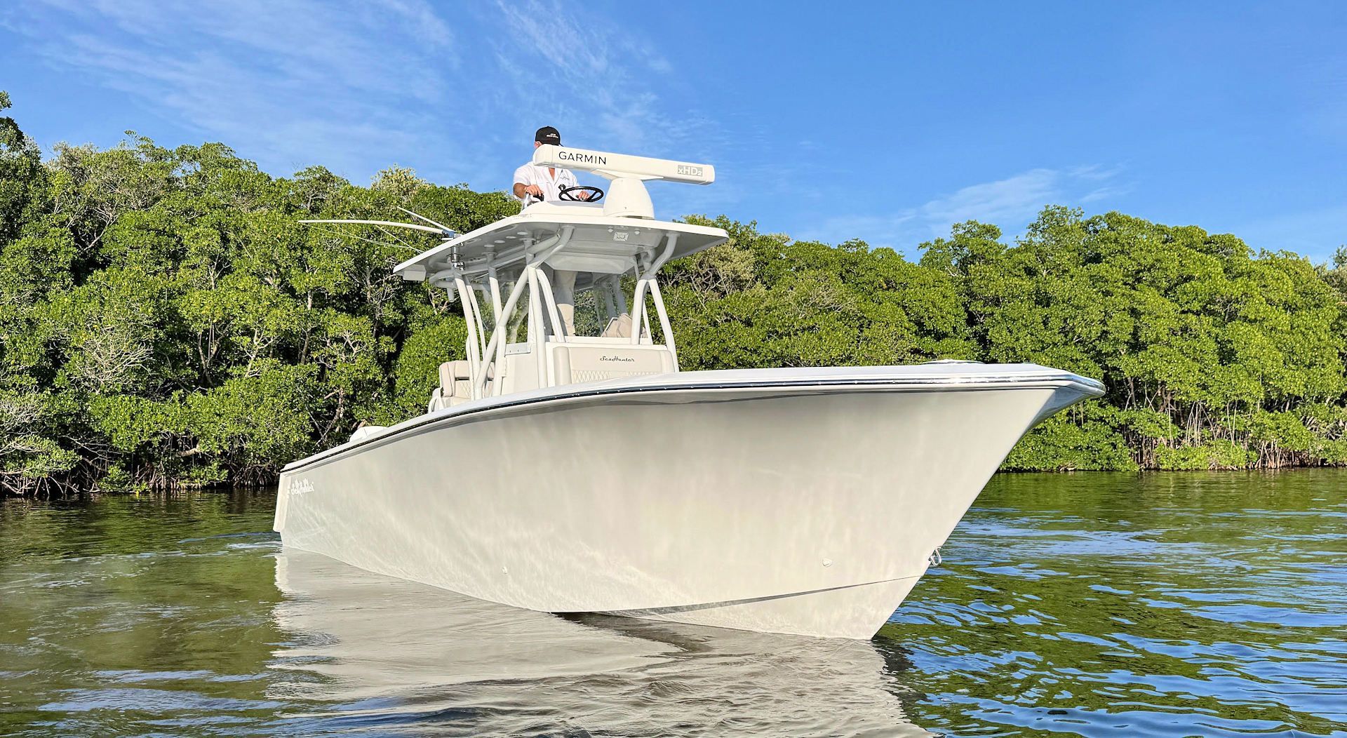 A SeaHunter center console boat moves through shallow water in front of a dense, green mangrove forest under a clear sky.