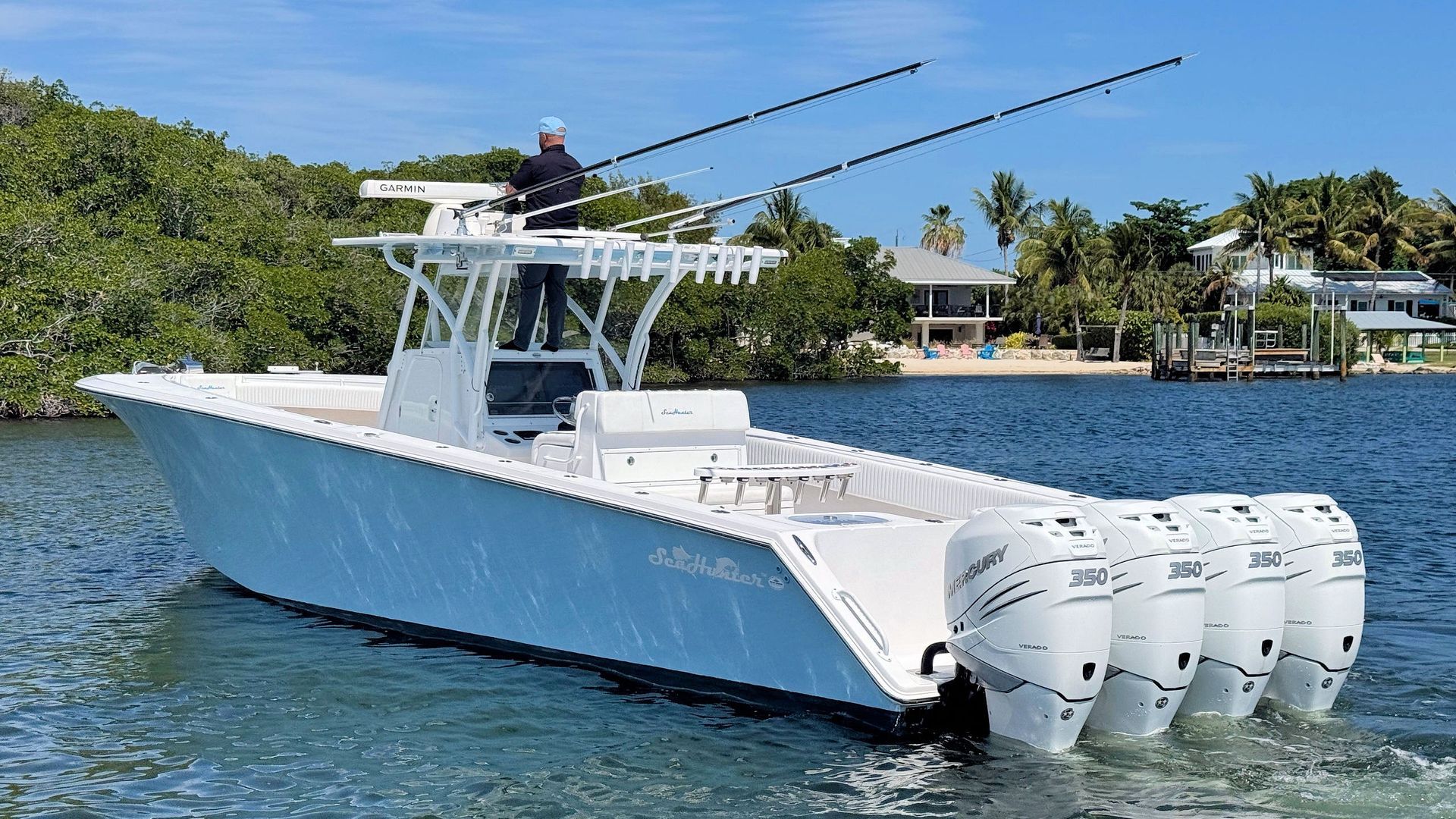 White center-console boat with triple outboard engines on calm blue water near a tropical shoreline.
