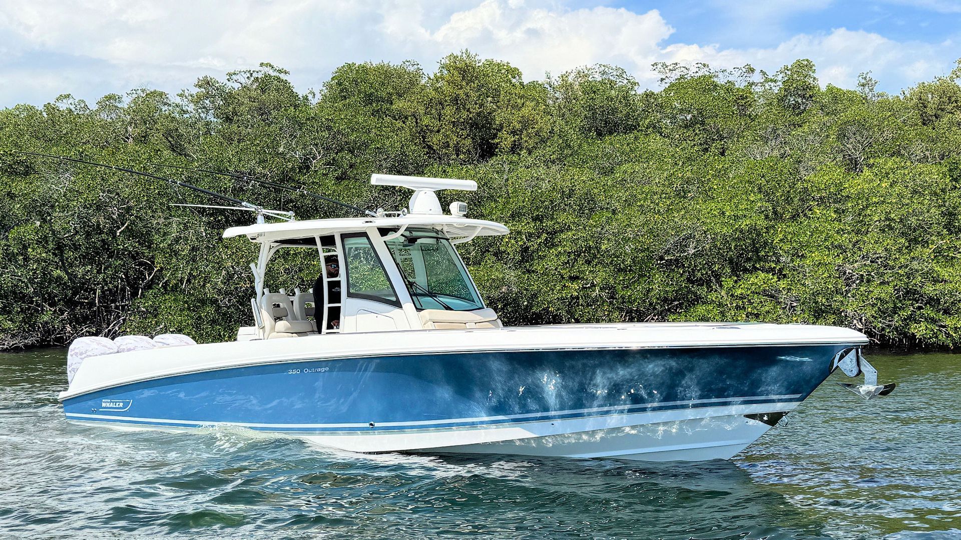 Blue and white Boston Whaler center console boat on choppy water near a mangrove shoreline