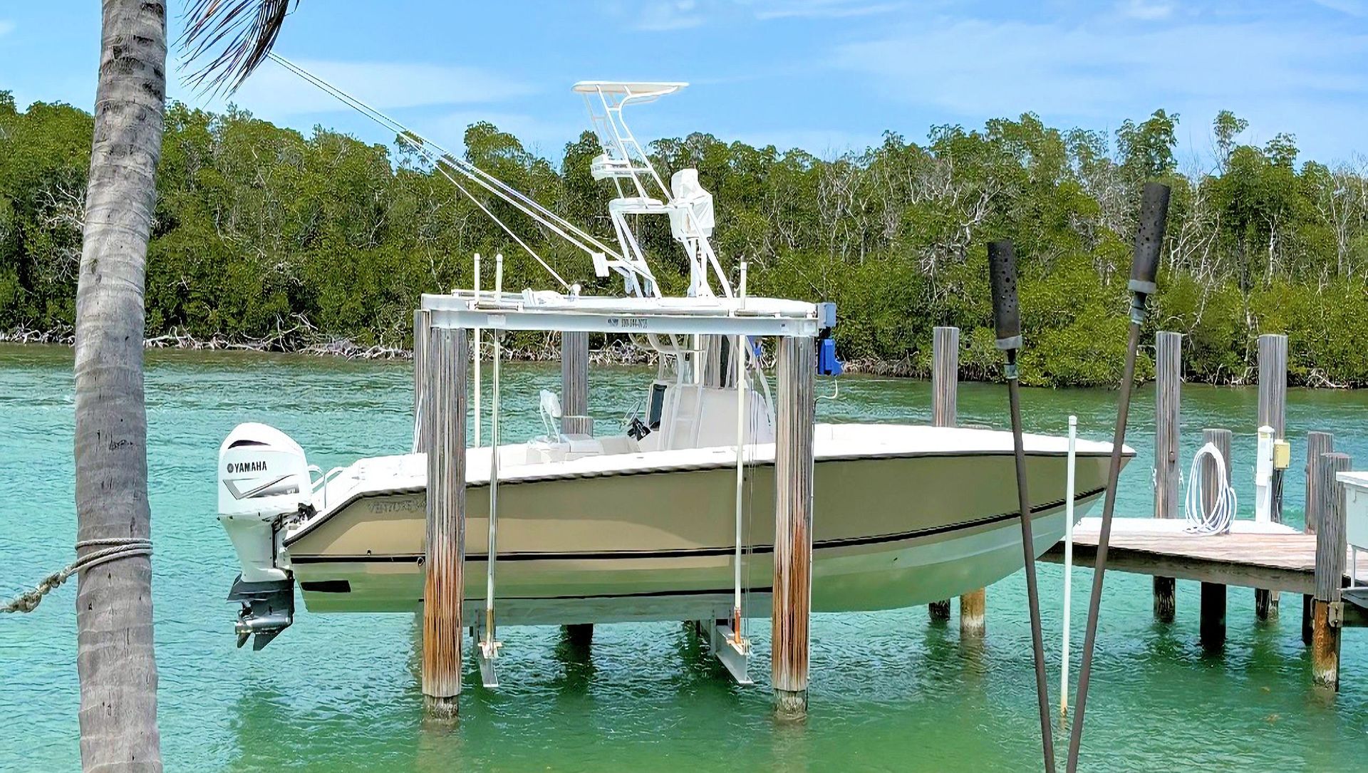 White and yellow center console docked at a wooden pier in clear turquoise water, with trees in the background