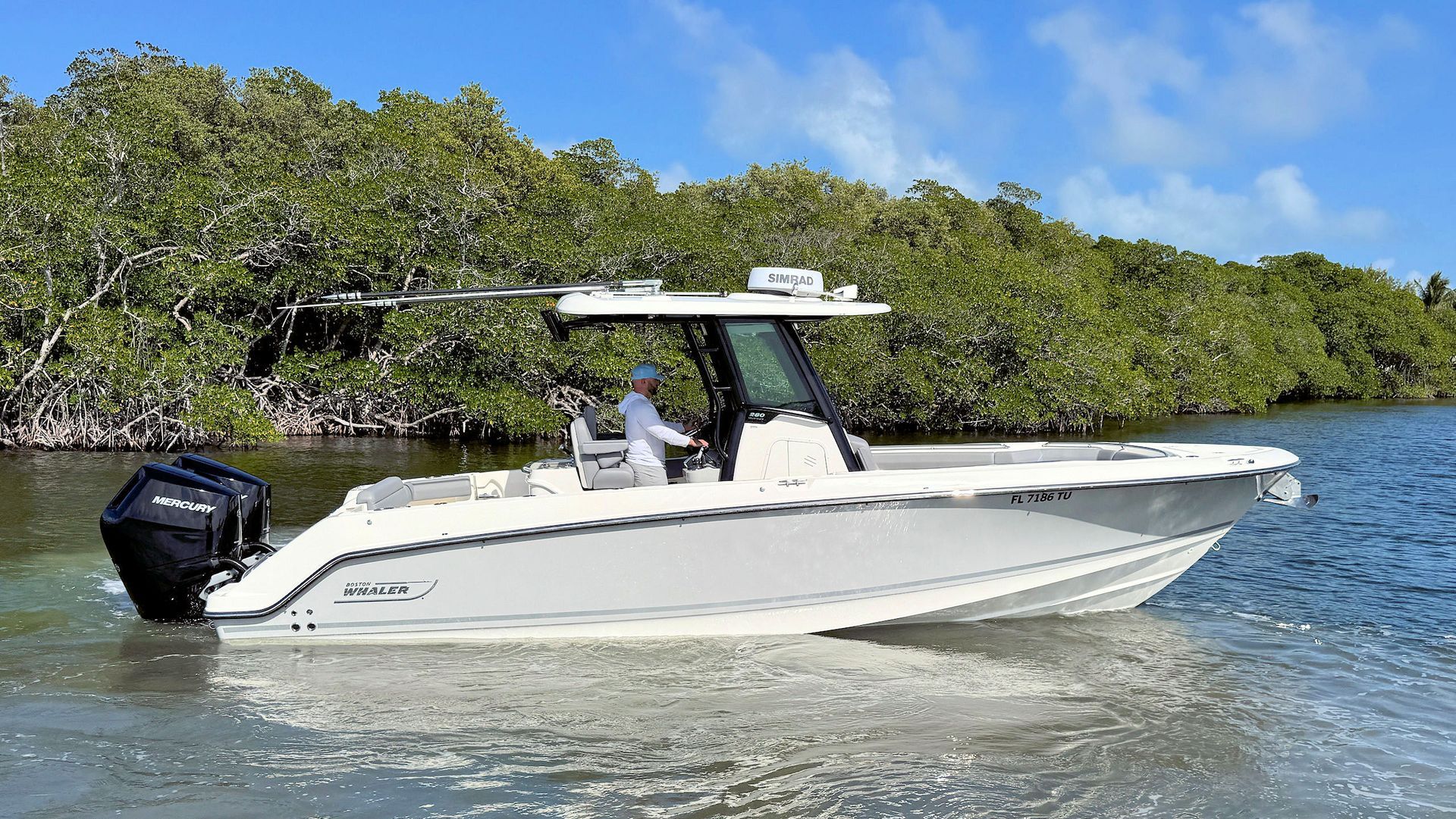 A white center-console motorboat cruises through shallow water near mangroves on a sunny day.