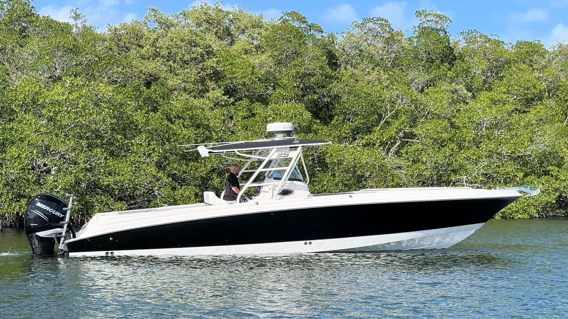 A white and black center console boat cruising through calm water alongside a lush mangrove shoreline.