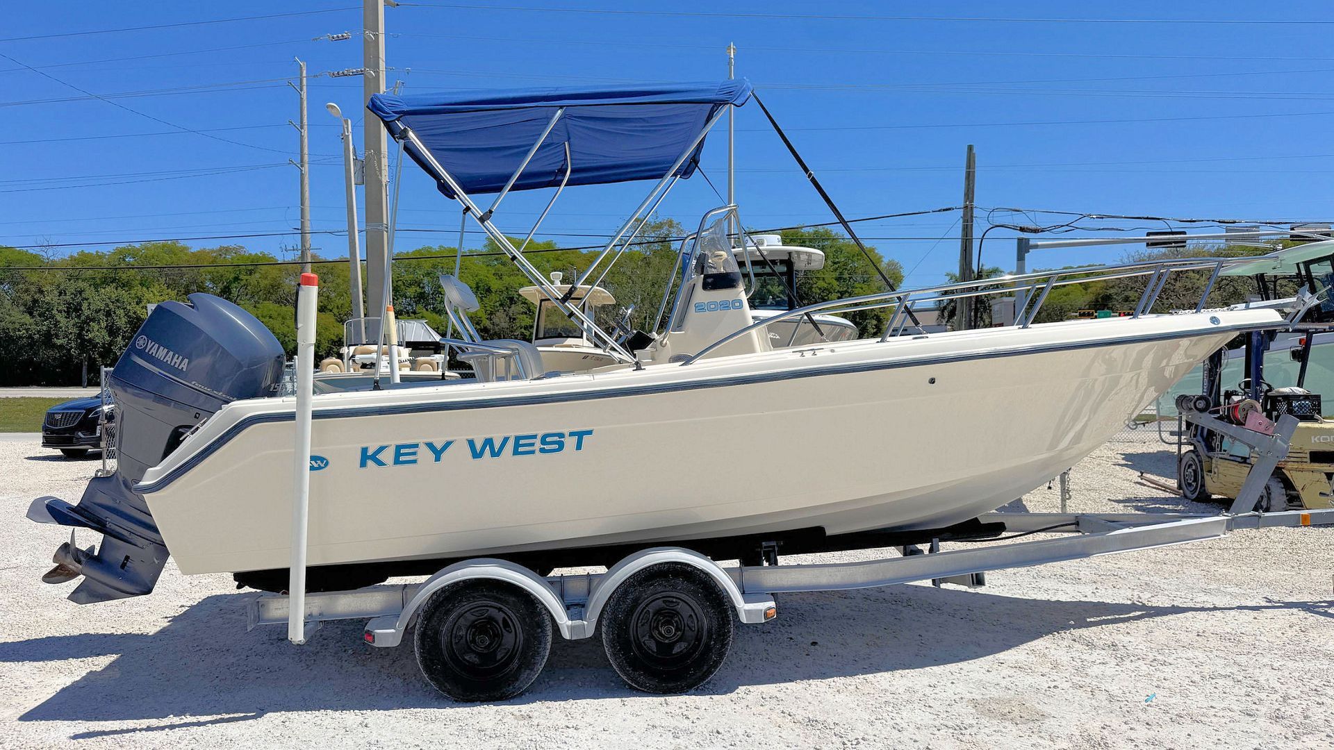 White Key West boat on a trailer at a gravel lot under a blue sky.