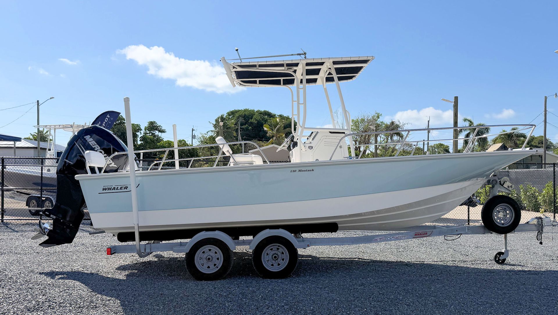 Light blue and white center console boat  on a trailer at a boat yard with an outboard motor and T-top canopy.