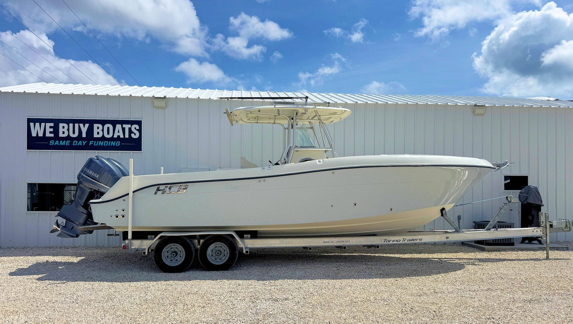 White center-console boat on a trailer outside a boat dealership with a “We Buy Boats” sign