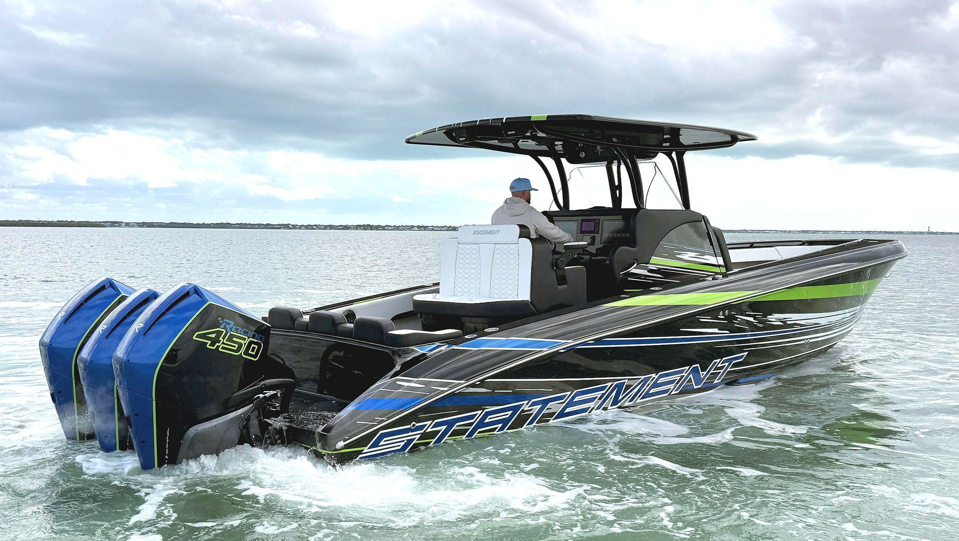 A person steering a high-performance center console boat with three blue outboard motors on a cloudy day at sea.