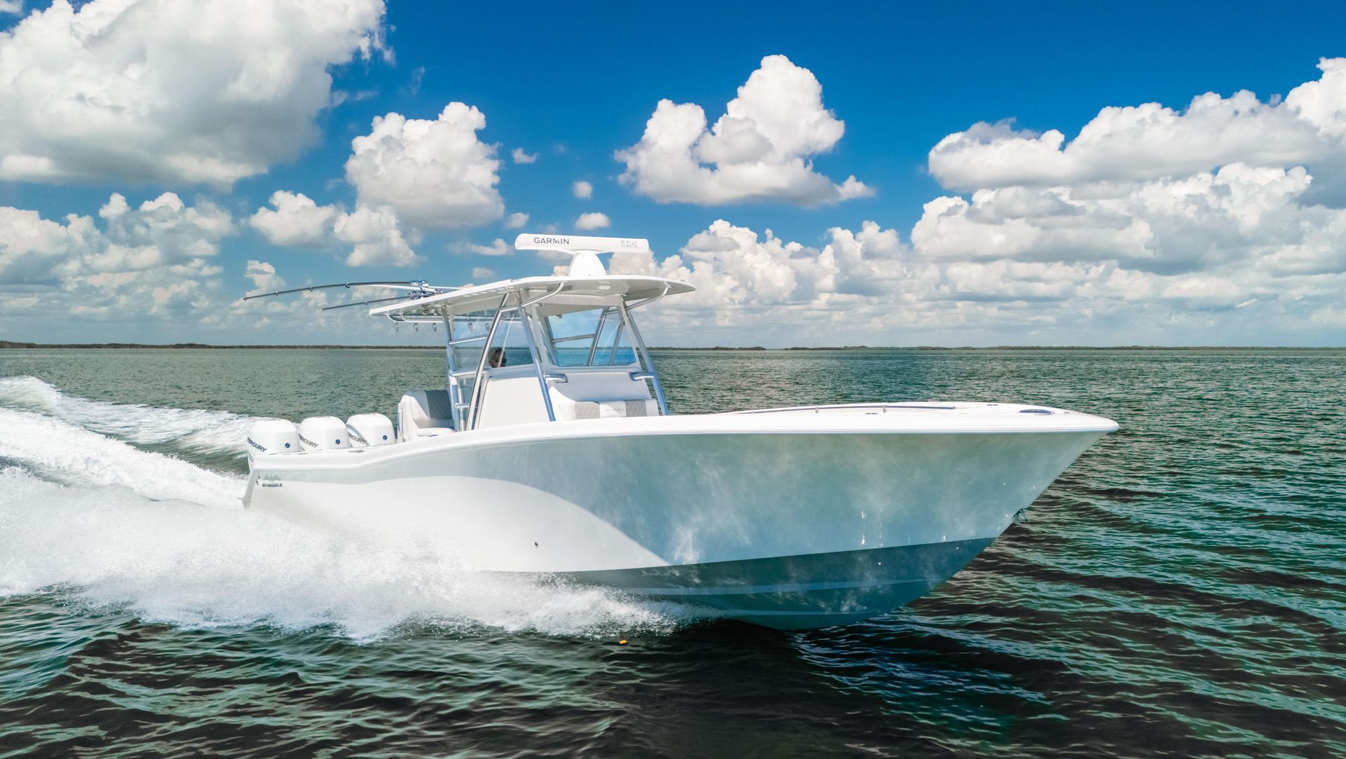 A white center console motorboat speeding through blue water under a bright, partly cloudy sky.