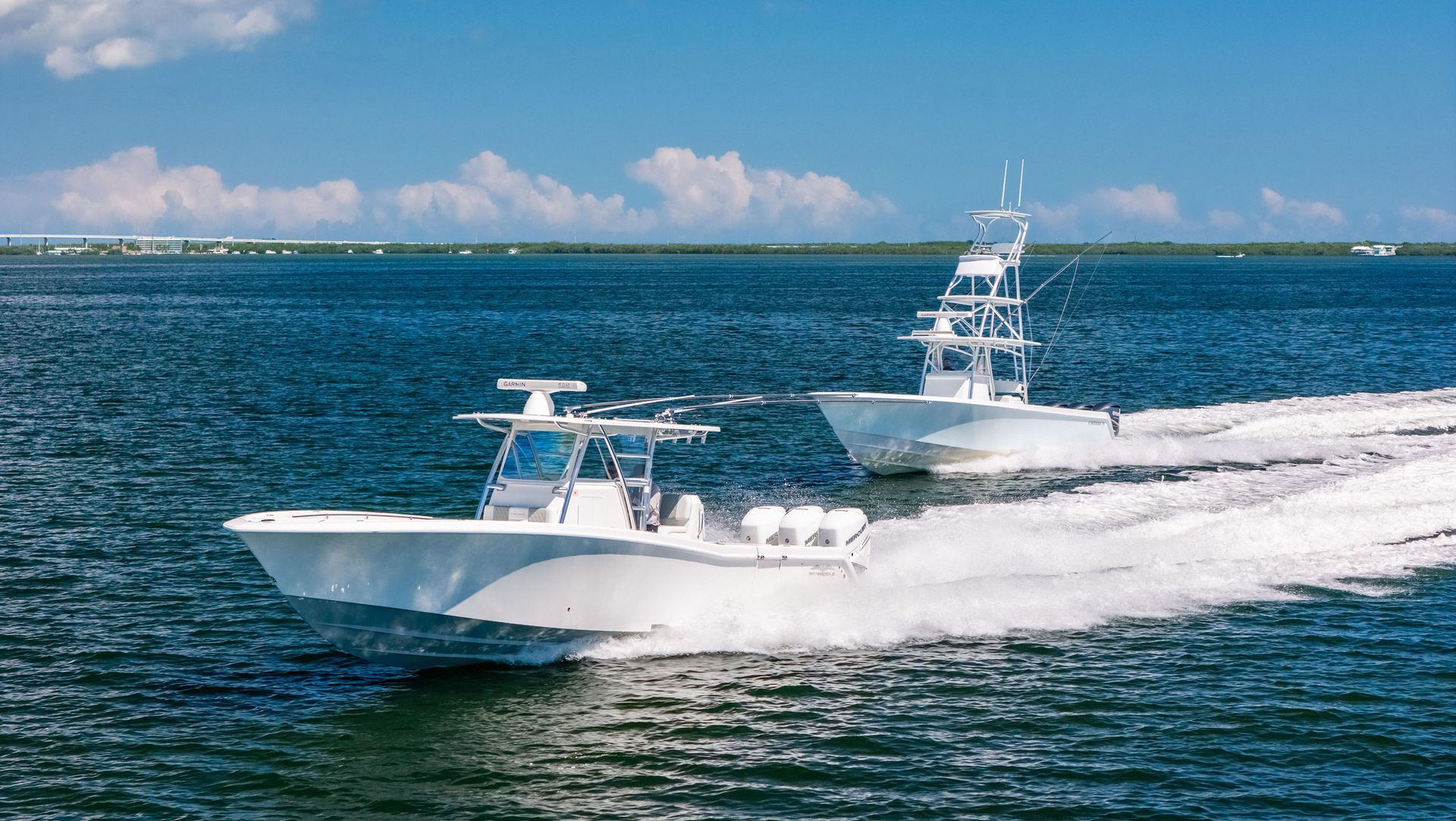 Two white center console boats traveling across blue water under a bright sky, creating white wakes behind them.