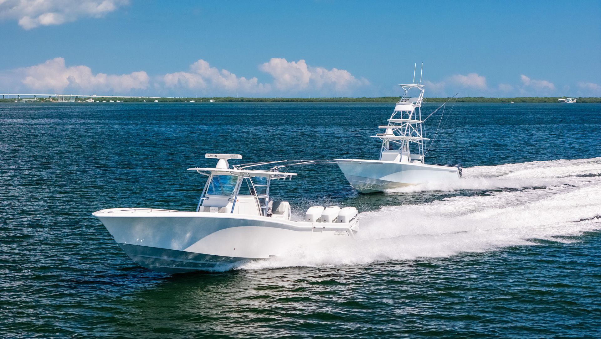 Two white powerboats with outboard motors speeding across the ocean under a clear blue sky.
