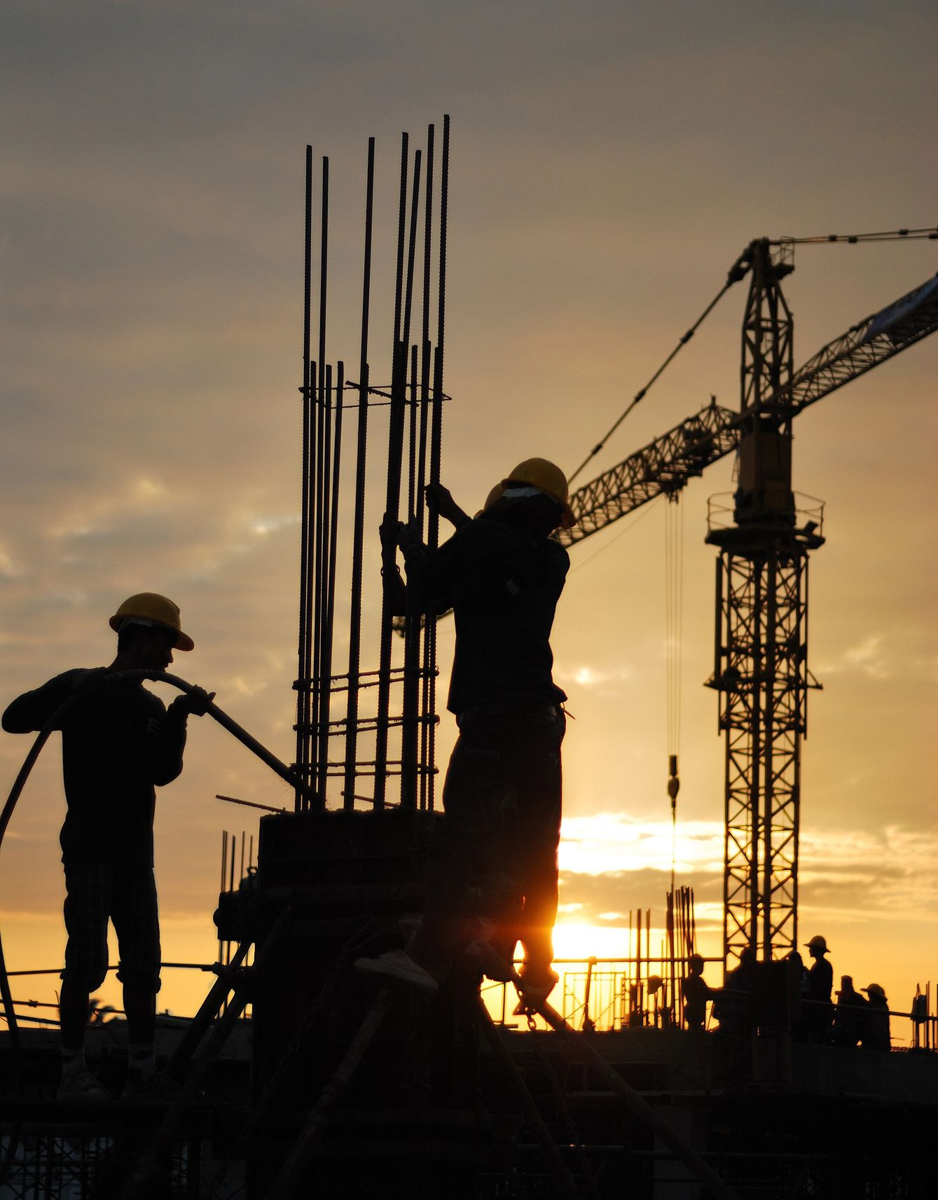Obreros de la construcción recortados contra una puesta de sol, trabajando en un edificio con una grúa.