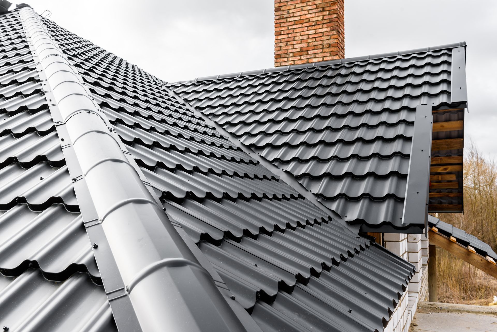 Gray tiled roof with a brick chimney on a house exterior