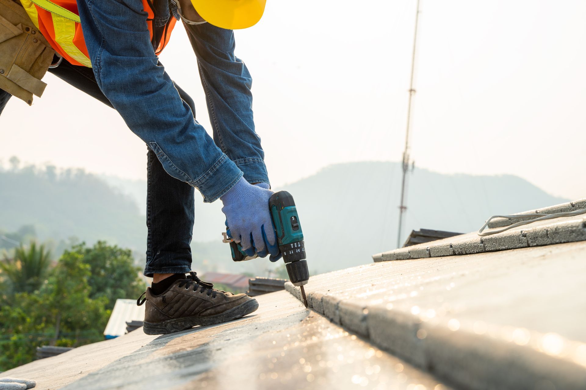 Worker using a power drill to fasten metal roofing panels on a rooftop.
