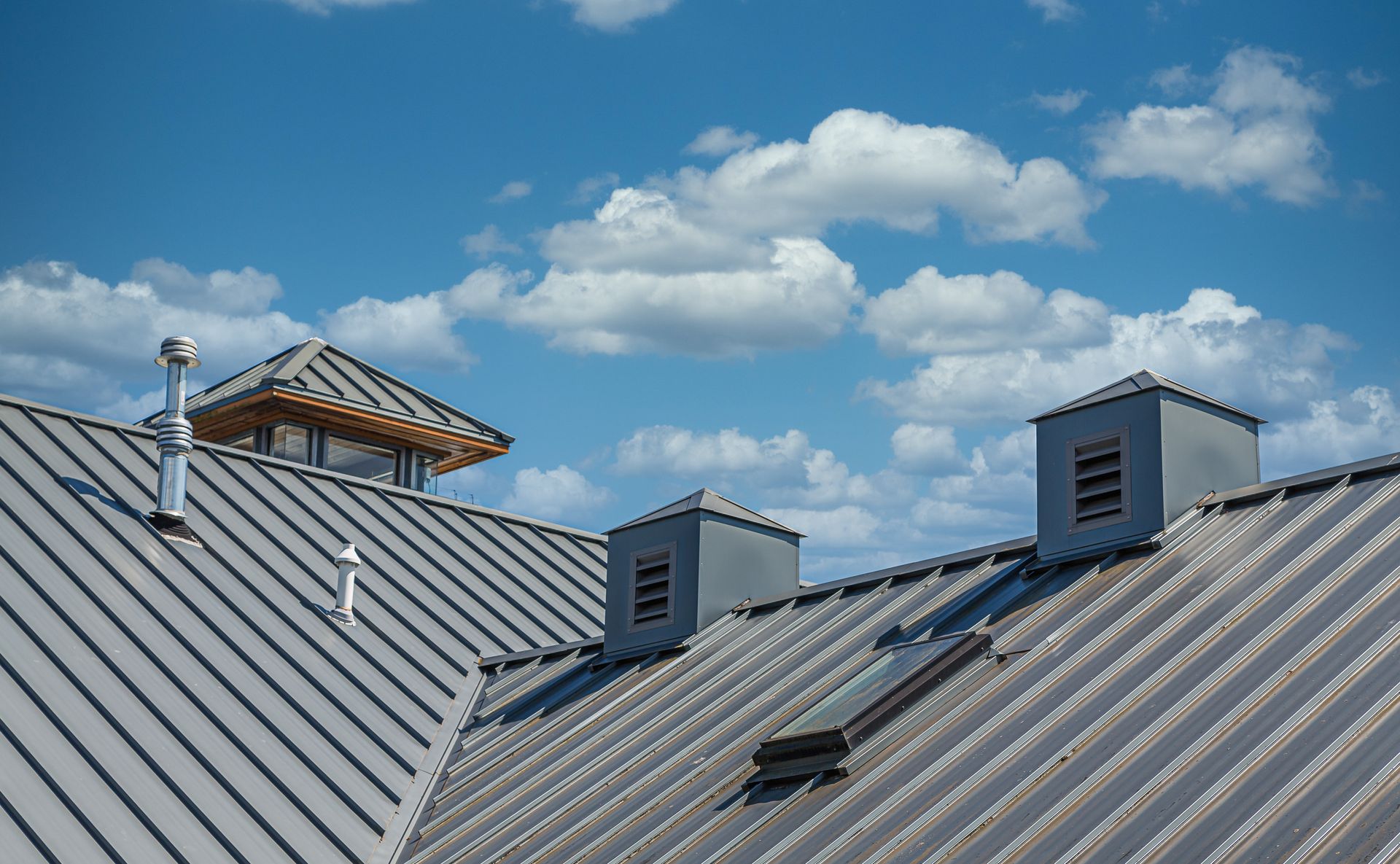 Metal rooftops with vent chimneys under a bright blue sky with scattered clouds