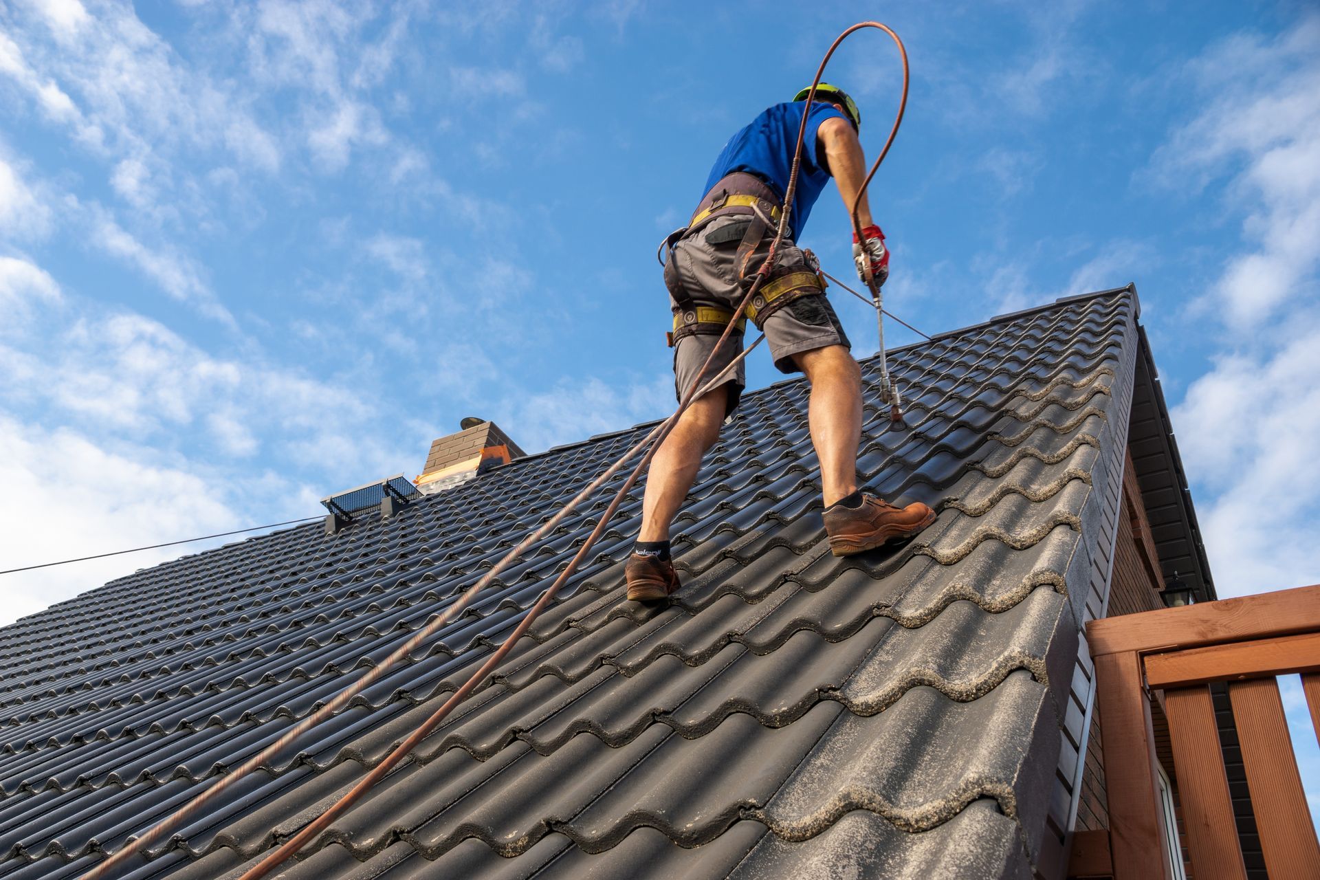 Worker on a steep roof using a safety harness and rope under a blue sky