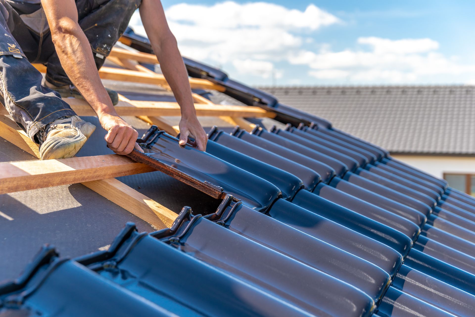 Worker installing blue roof tiles on a house roof