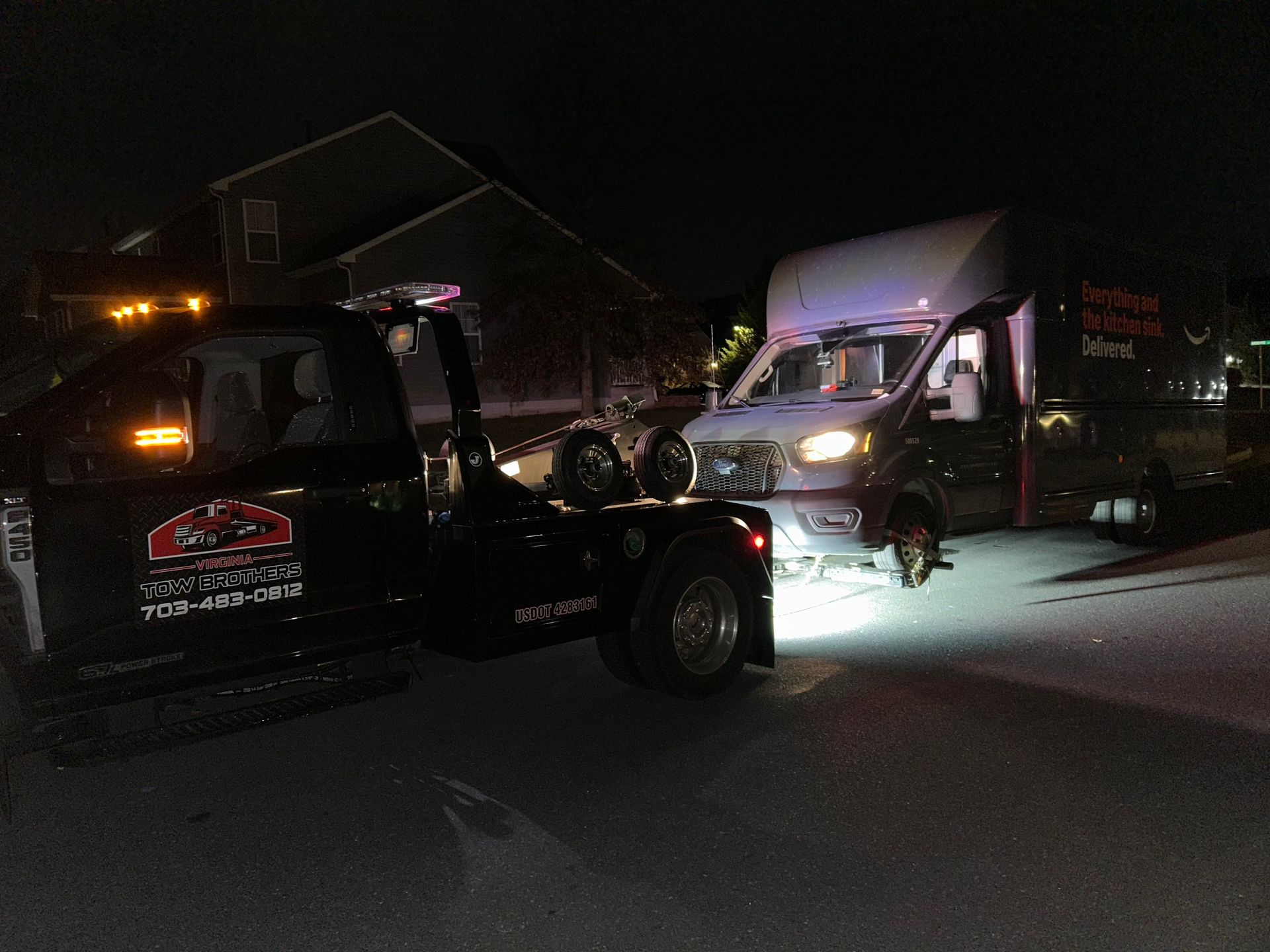 Two tow trucks are parked next to each other in a driveway at night.
