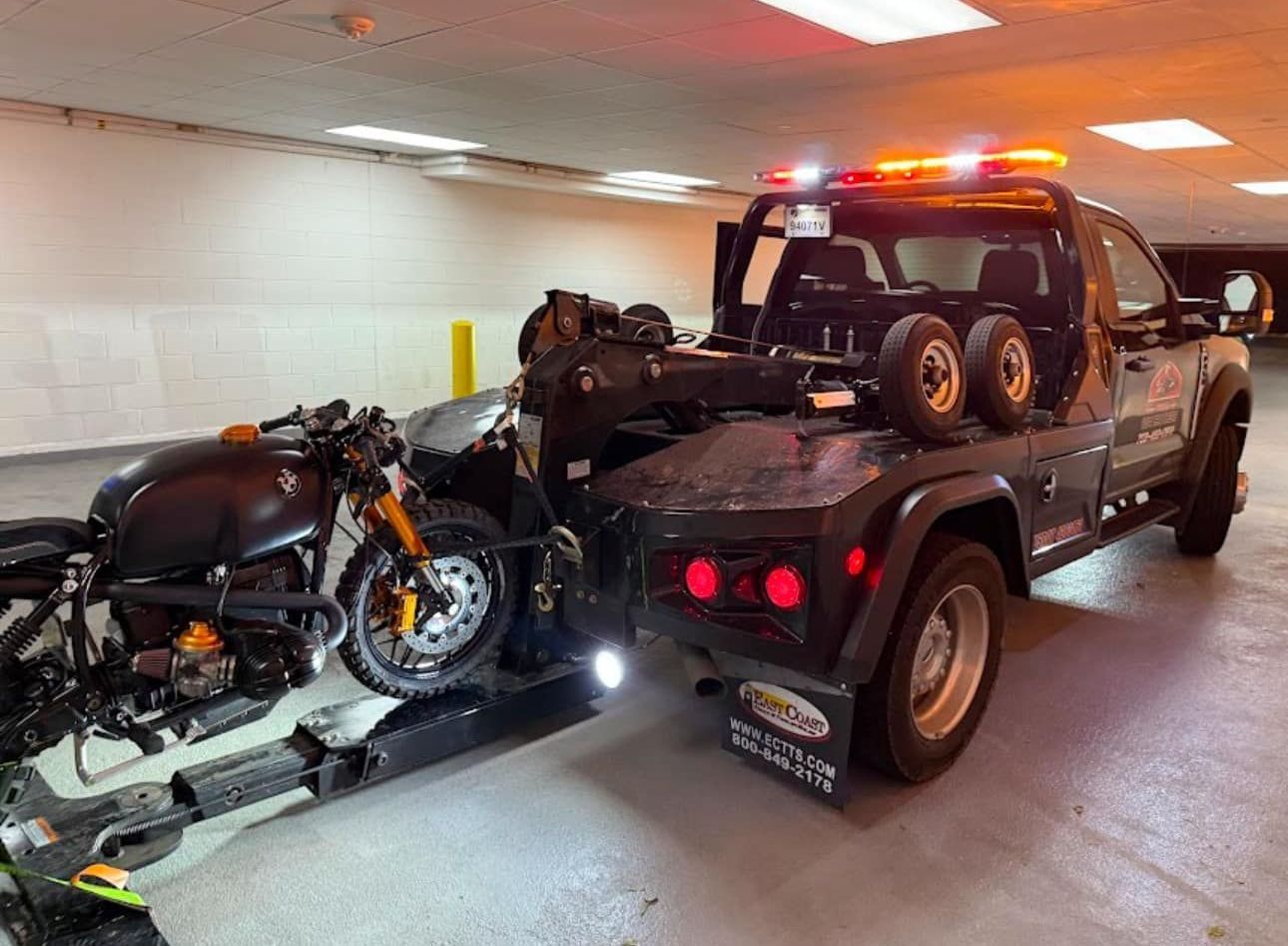 A tow truck is towing a motorcycle in a parking garage.