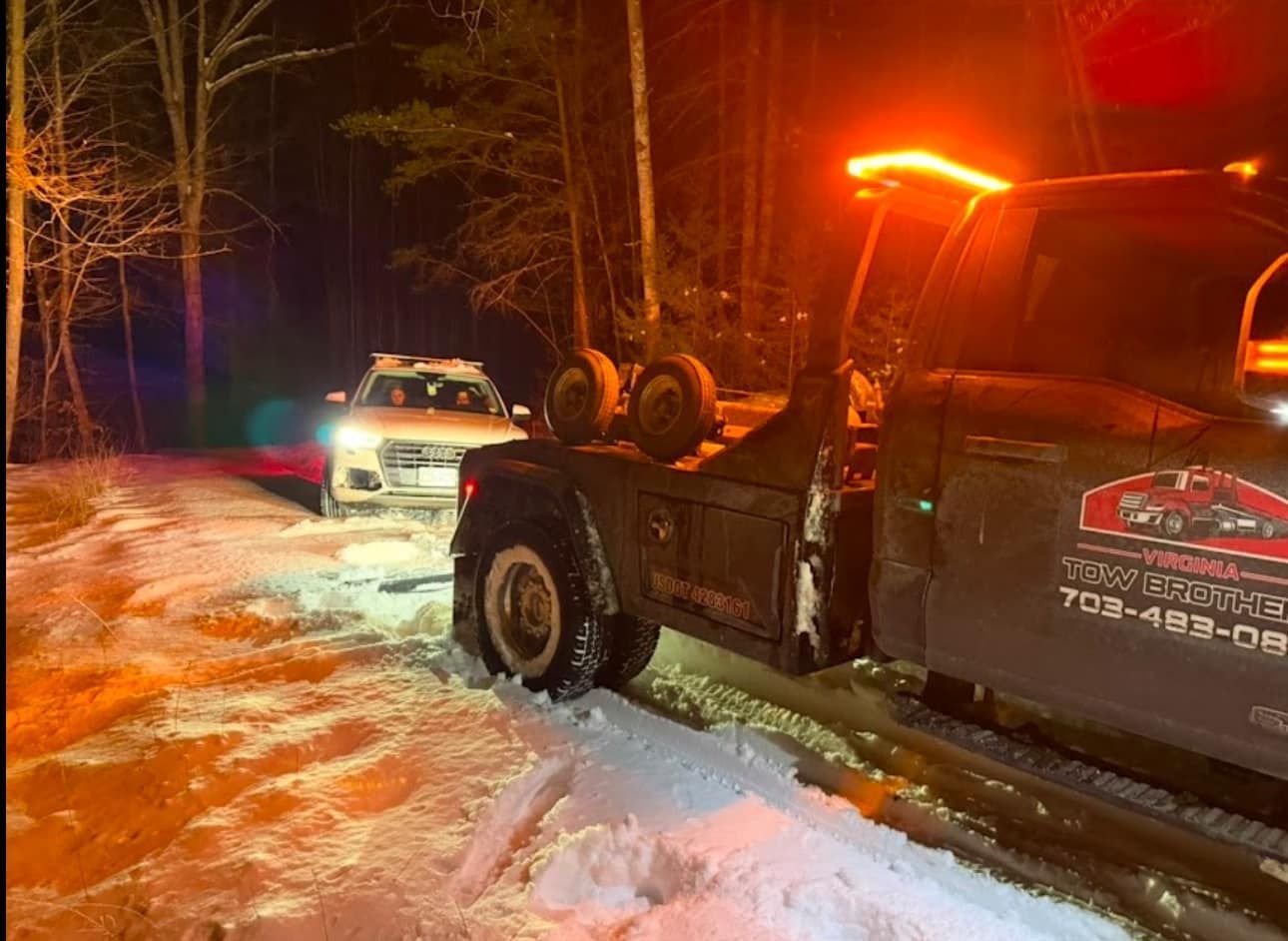 A tow truck is towing a car in the snow at night.