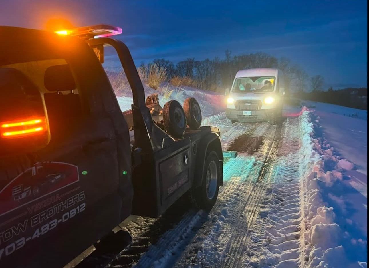 A tow truck is towing a van in the snow.
