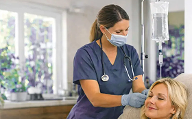 Person receiving intravenous fluids. Medical staff, gloved hands; arm on pillow with IV line and bandage.
