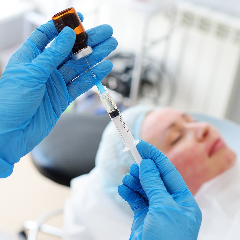 Person receiving lip filler injection; blue gloved hands holding syringe near lip.