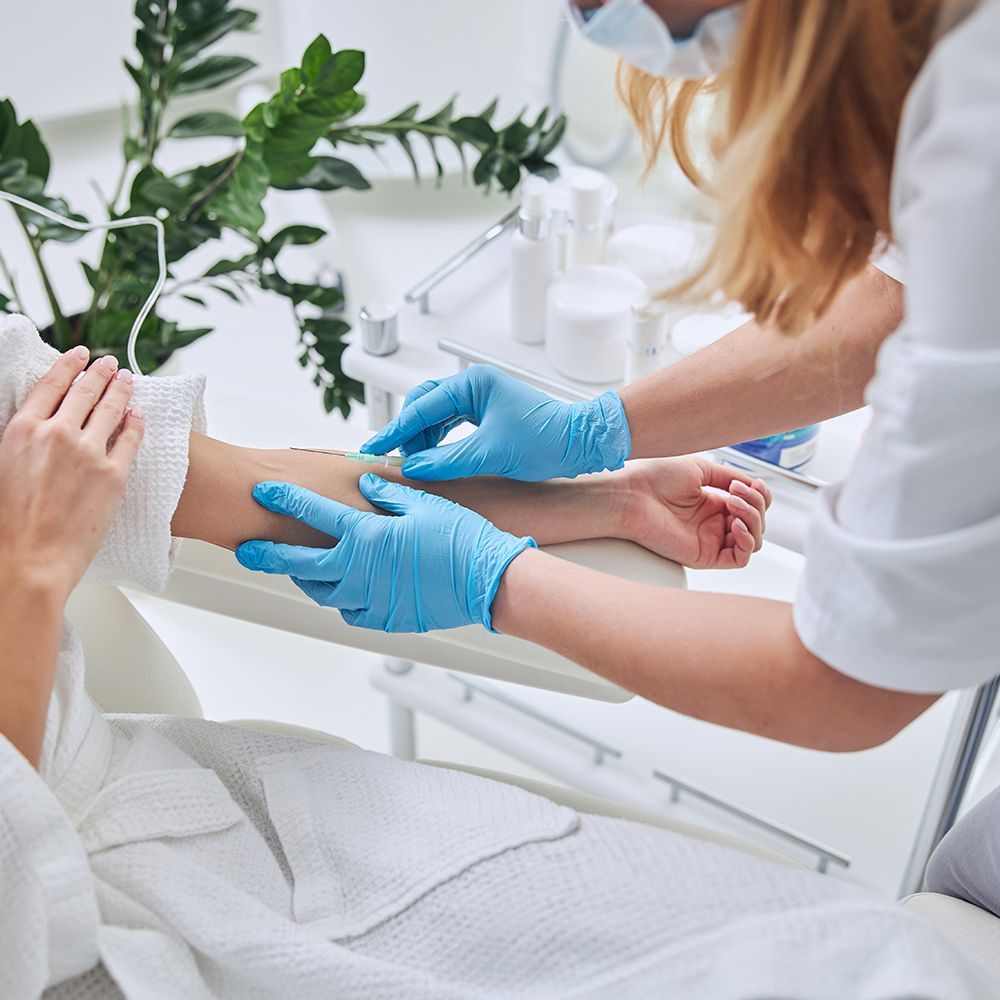 A healthcare worker wearing gloves prepares a patient's arm for a medical procedure, in a clinical setting.