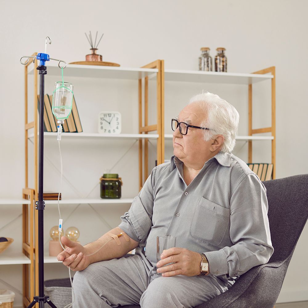 Man receiving IV therapy in a home setting; sitting in a chair, looking away.
