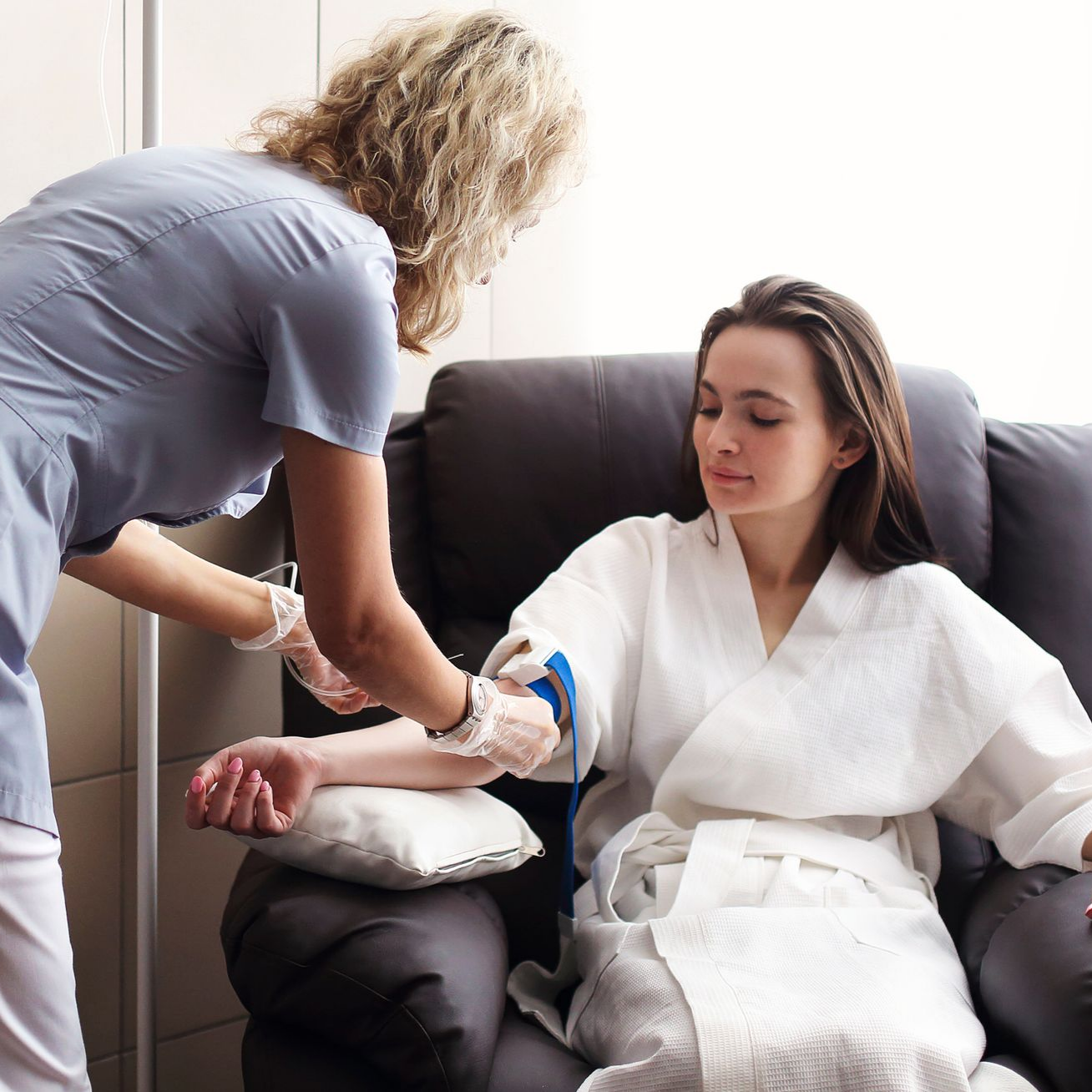 Person receiving intravenous fluids. Medical staff, gloved hands; arm on pillow with IV line and bandage.