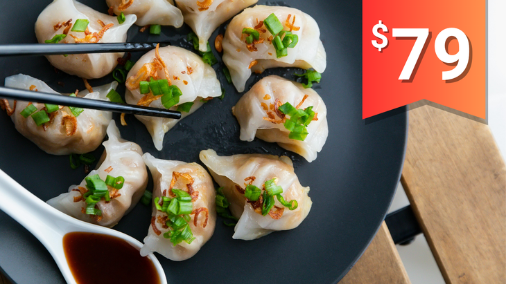 A plate of steamed pork dumplings topped with green onion served with a side of soy sauce.