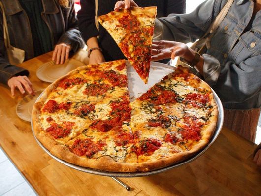 A slice of Nonna Maria pizza from Bleecker Street Pizza, known for its crispy crust and fresh tomato basil topping.