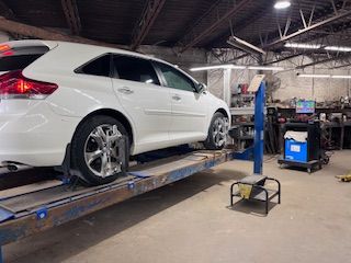 A man is standing next to a car on a lift in a garage.