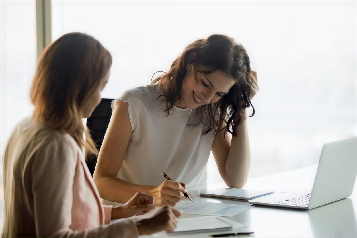Two women are sitting at a table looking at a laptop.