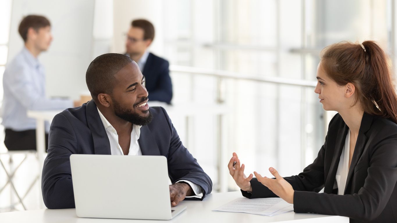 A man and a woman are sitting at a table with a laptop.