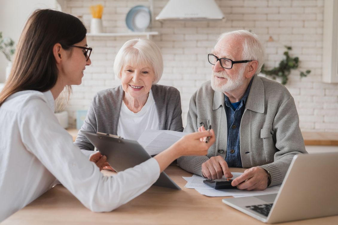 An elderly couple is sitting at a table with a woman talking to them.