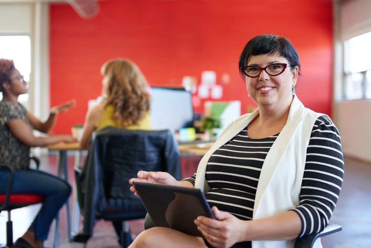 A woman is sitting in a chair holding a tablet computer.