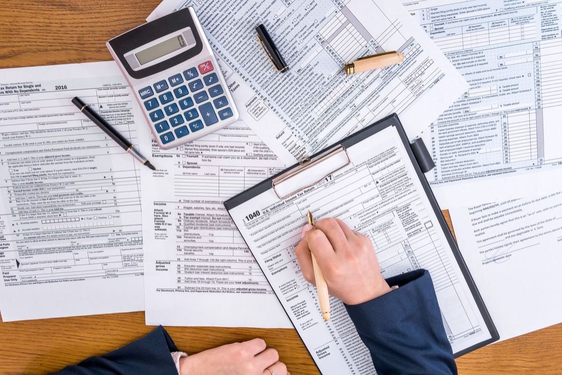 A person is sitting at a desk filled with papers and a calculator.