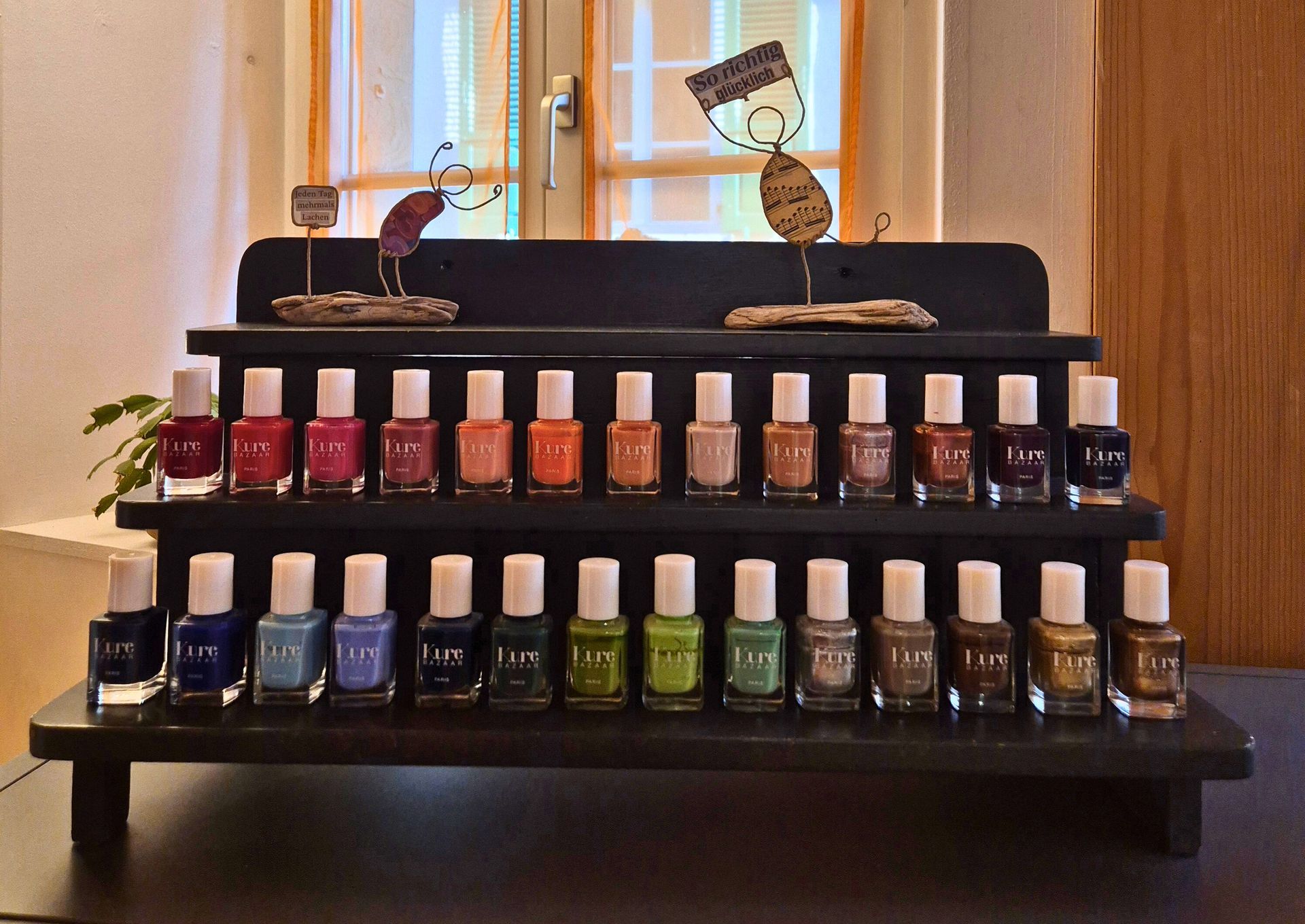 Schwarzes, gestuftes Display mit verschiedenen Nagellackflaschen von Essie vor einem Fensterhintergrund.