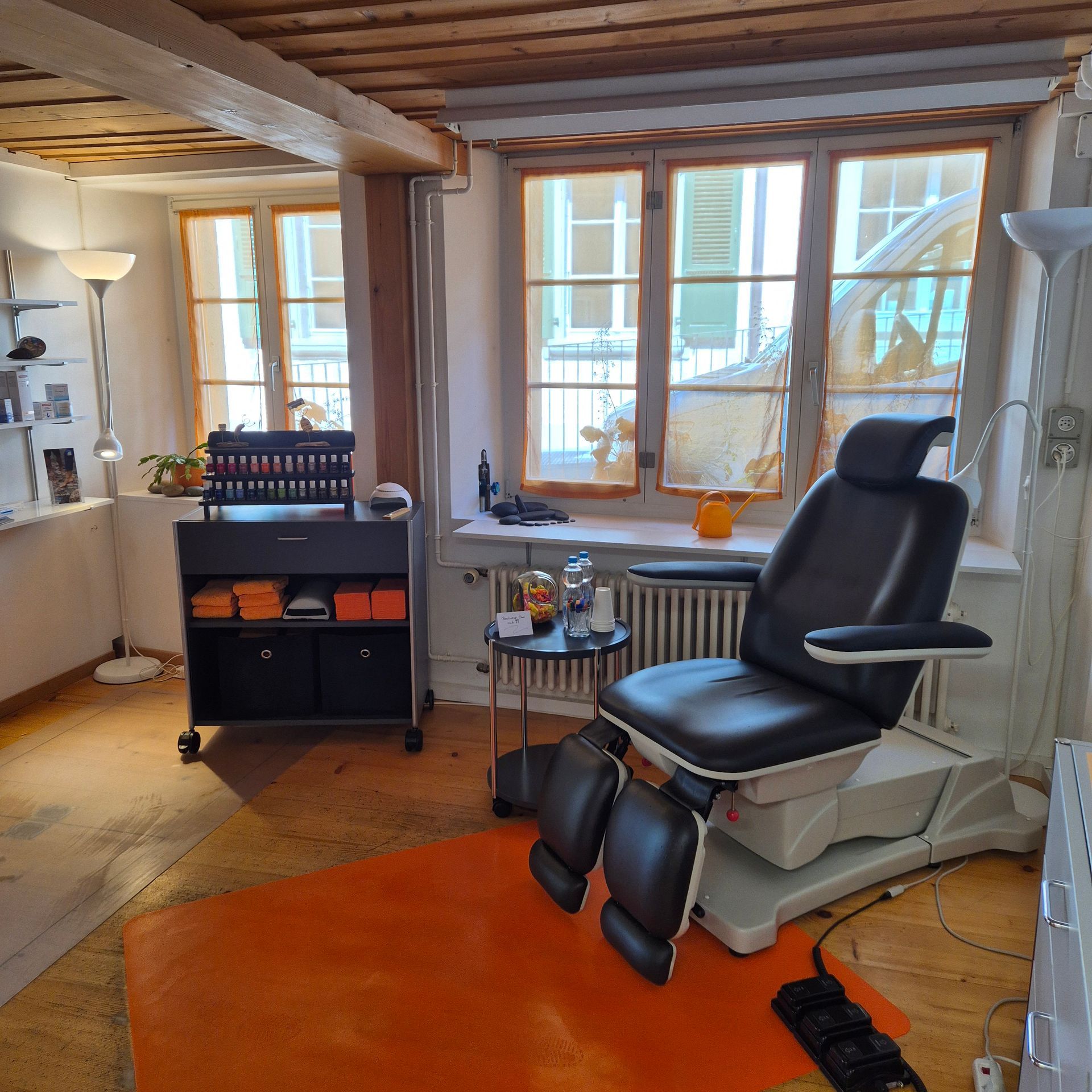 Ein Zahnarztpraxiszimmer mit Patientenstuhl, orangefarbenem Teppich, Fenstern und Lagerwagen.