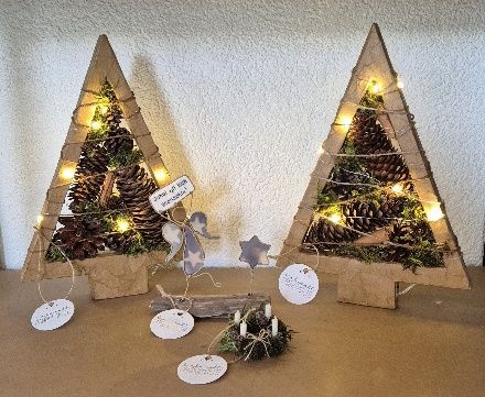 Zwei Weihnachtsbaumdekorationen aus Pappe mit Lichtern, Tannenzapfen und kleinen Ornamenten.