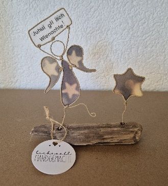 Engelsfigur aus Draht mit Stern, die ein Schild mit der Aufschrift „Juhui! gib is Wiachnachte!“ hält, und Sockel aus Treibholz.