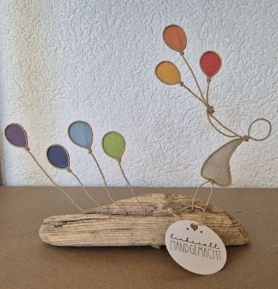Skurrile Metallfigur mit bunten Glasballons, befestigt an einem Treibholzsockel.
