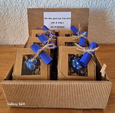 Geschenkkorb mit Pralinen, blauen, mit Bindfaden zusammengebundenen Schriftrollen und einer Grußkarte.