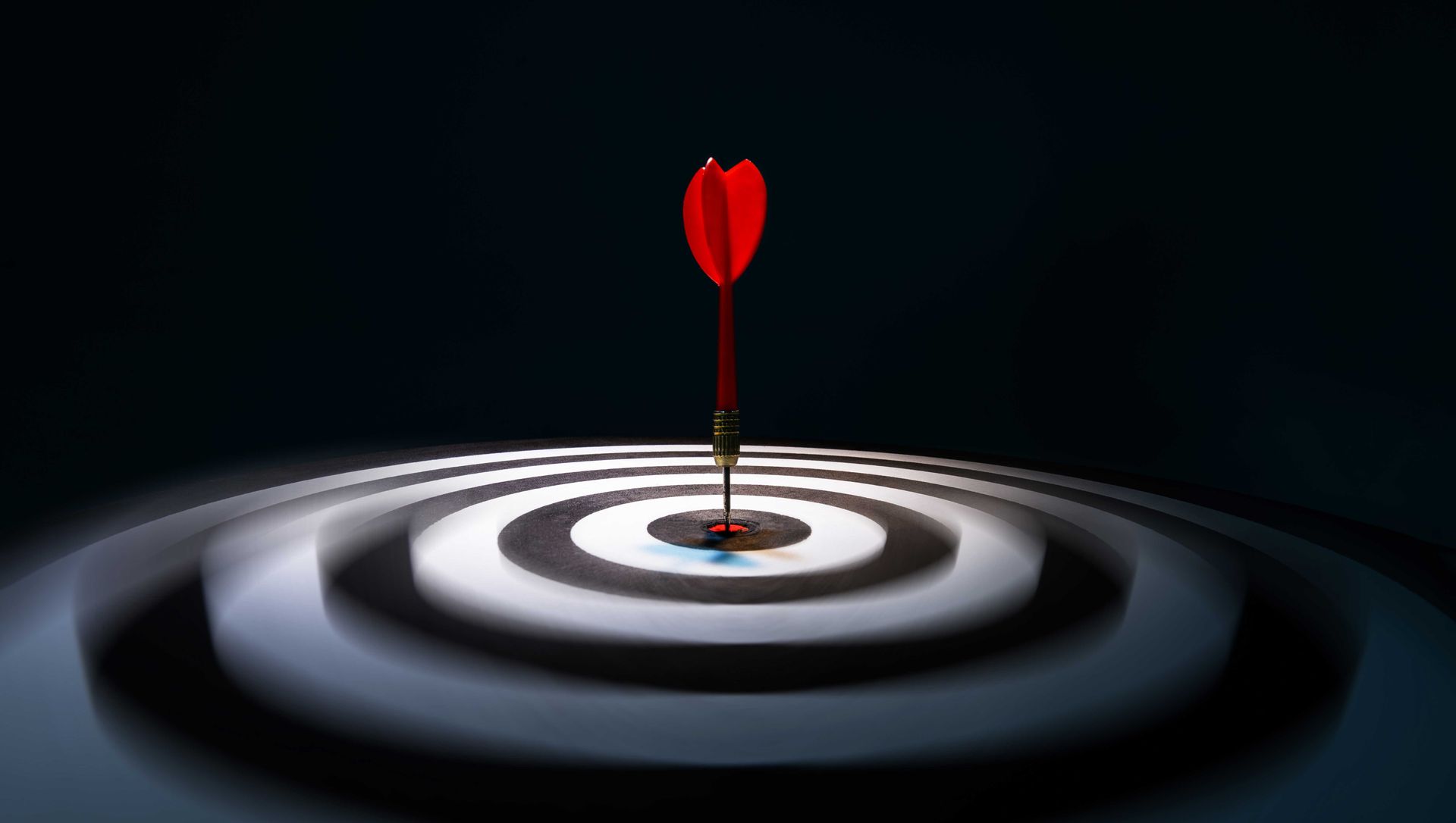 A red dart is hitting the center of a target.