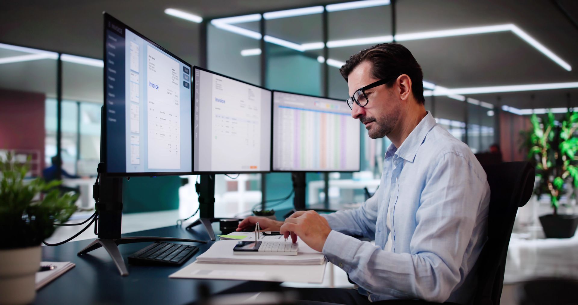 A man is sitting at a desk in front of three computer monitors.